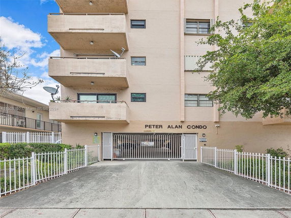 Front view of a multi-story condo building with balconies and gated entrance.