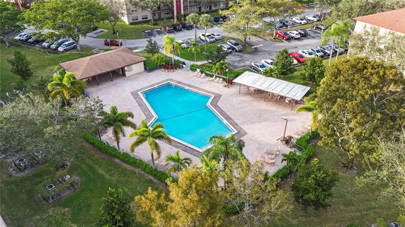 Aerial view of an outdoor swimming pool area surrounded by trees and adjacent to a parking lot.