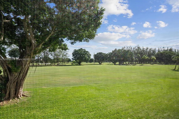 A scenic view of a large green field with trees under a blue sky.