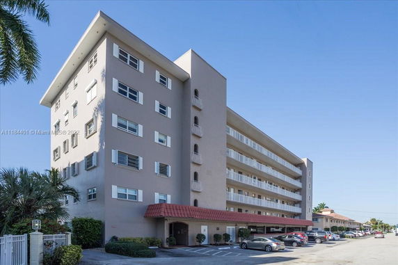 Front view of a multi-story apartment building with balconies and a red-tiled entrance canopy.