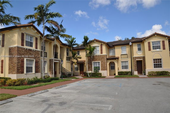 Front view of a two-story townhouse complex with beige stucco and stone accents.
