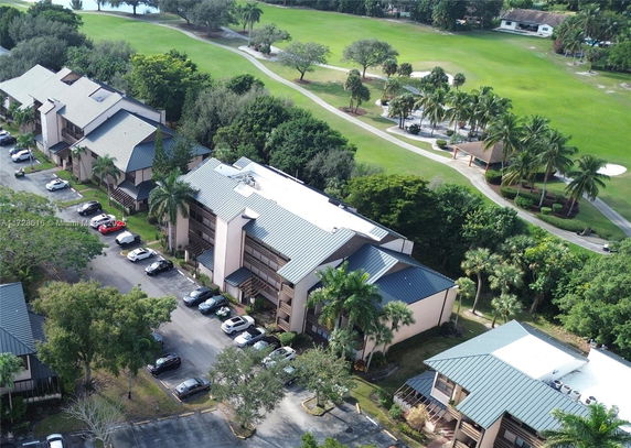 Aerial view of residential buildings surrounded by green landscape and parking area.