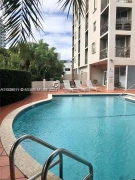 Outdoor swimming pool area adjacent to a multi-story building with lounge chairs.