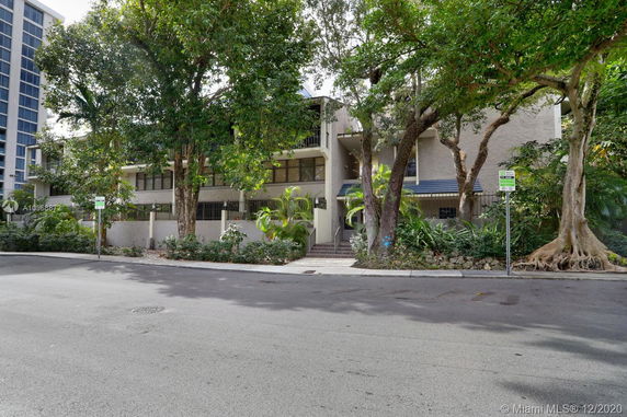 Front view of a multi-story building with large trees at the entrance.