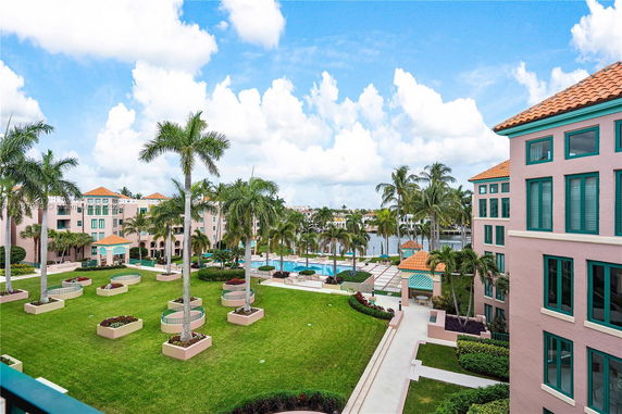 View of a resort-style complex with multiple buildings, swimming pools, and landscaped gardens featuring palm trees.