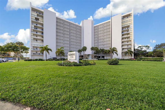 Front view of a multi-story building with balconies and a large grassy area in front.