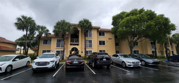 Front view of a multi-story building with balconies and a parking area in front.