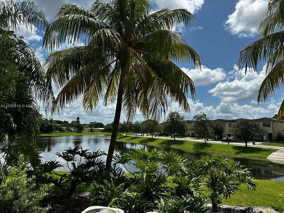 View of a residential area with houses by a waterway, surrounded by palm trees and greenery.