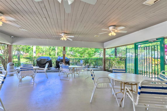 Covered outdoor seating area with tables, chairs, ceiling fans, and green surroundings.