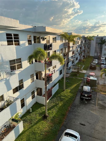 Side view of a multi-story apartment building with balconies and parked cars below.
