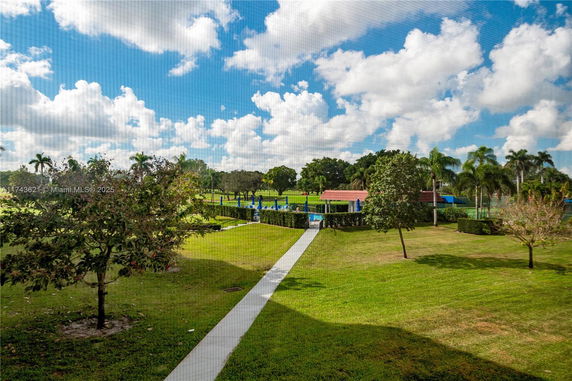 View of a landscaped area with trees, lawns, and a pathway leading to a building with a red roof.