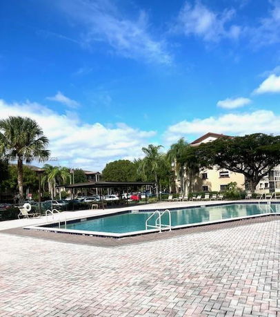 Outdoor swimming pool with surrounding palm trees and buildings.