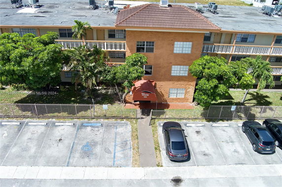 Front view of a three-story brick building with a red awning above the entrance and parking spaces in front.