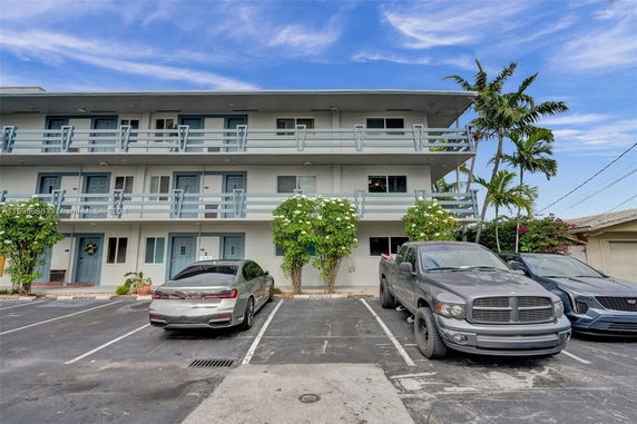 Front view of a three-story residential building with balconies and parking spaces.