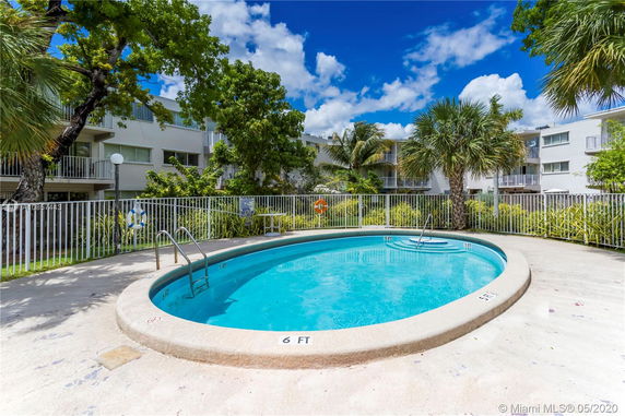 Outdoor round swimming pool surrounded by buildings and palm trees.