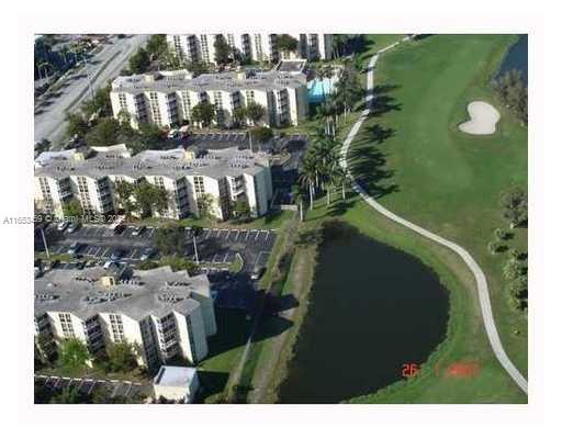 Aerial view of a complex of multi-story buildings beside a golf course and a water body.