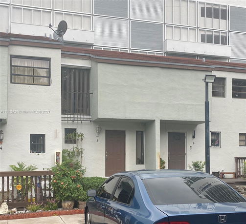 Front view of multi-story residential building with two entrances and a parked car in front.
