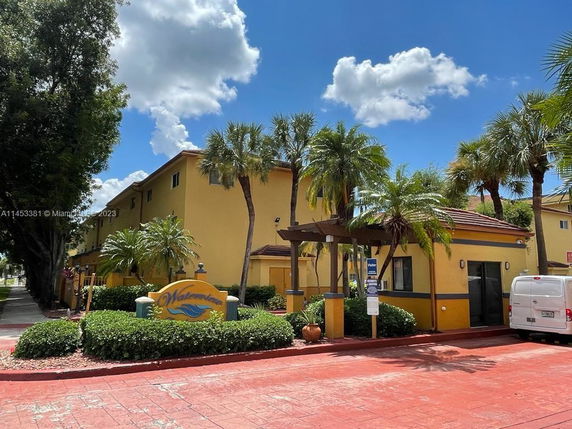 Front view of a yellow building with two stories and palm trees in front.