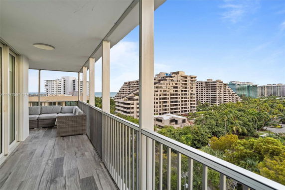 Balcony view overlooking several multi-story buildings and a forested area, with a glimpse of the ocean in the background.