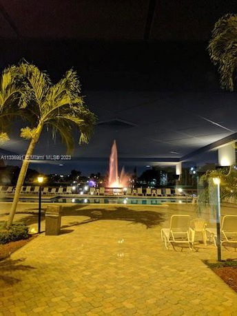 Nighttime view of a swimming pool area with a illuminated fountain in the background.