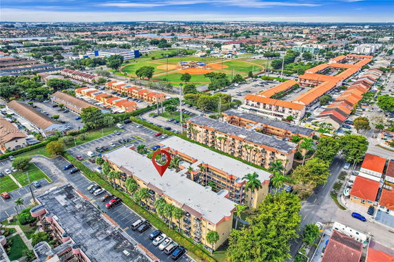 Aerial view of a residential area with multi-story buildings, parking lots, and a baseball field nearby.