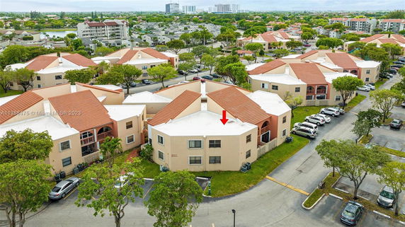 Aerial view of multiple residential buildings with red-tiled roofs and parking areas surrounded by trees.
