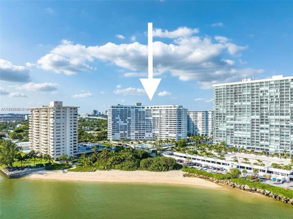 Aerial view of multiple high-rise buildings near a waterfront with a sandy beach.