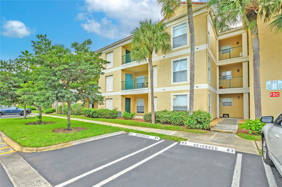 Front view of a three-story apartment building with balconies and reserved parking spaces.