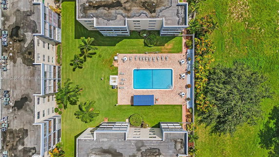 Aerial view of an outdoor swimming pool surrounded by sun loungers and integrated with nearby buildings.