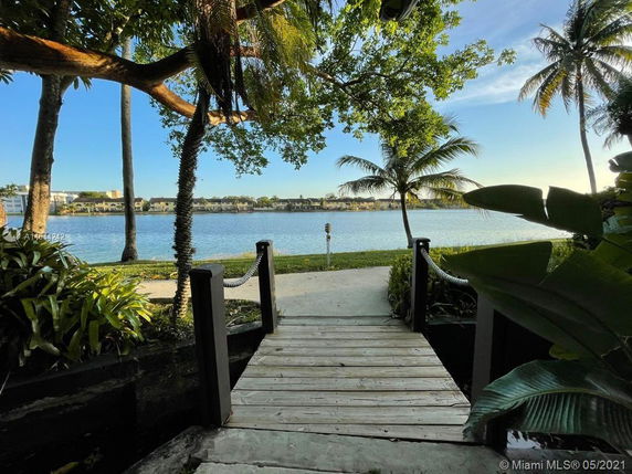 Deck path leading to a serene lake view with palm trees and distant houses.