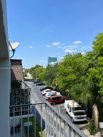 View from building over outdoor parking area with several vehicles and trees.