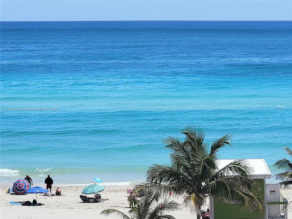 Beach scene with umbrellas, people relaxing, palm trees, and the ocean in the background.