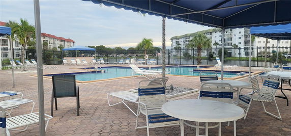 Outdoor swimming pool area with lounge chairs and tables under canopies.