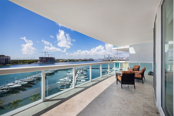 Balcony view overlooking a marina with boats and distant city skyline.