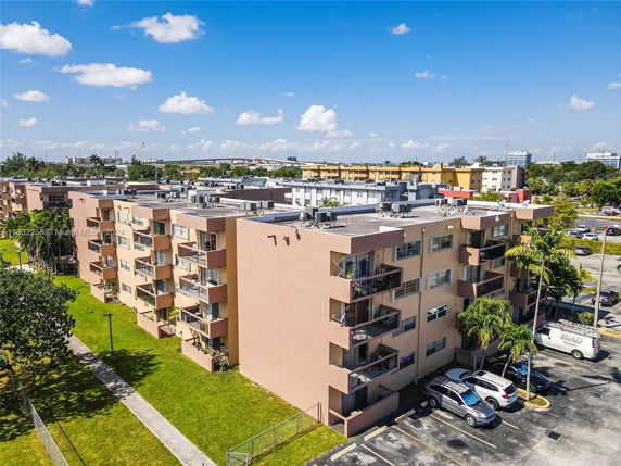 Aerial view of a multi-story apartment building with balconies, surrounded by a grassy area and parking lot.
