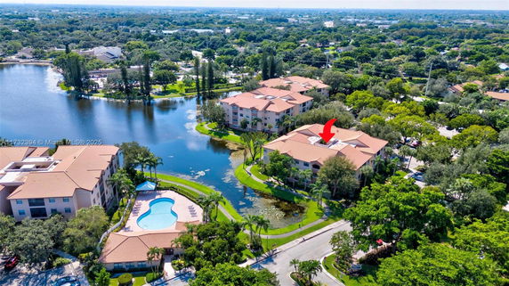 Aerial view of a complex with several buildings near a body of water and surrounding greenery.