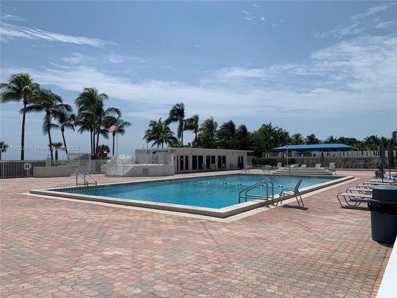 Outdoor swimming pool area with lounge chairs and palm trees.