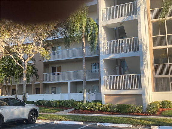 Front view of a multi-story apartment building with balconies and a parking area.
