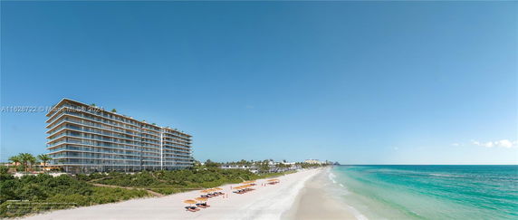 Angled view of a beachfront condominium building with glass balconies, next to a sandy beach and ocean.