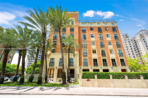 Front view of a multistory building with tall windows and palm trees.