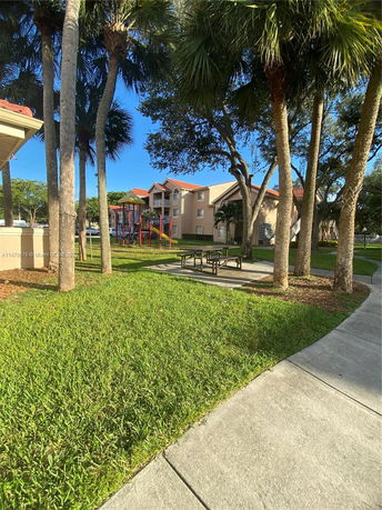 View of a building with a playground and picnic tables under trees.