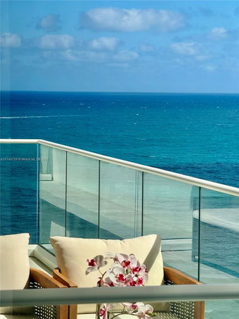Ocean view from a balcony with glass railing and comfortable seating.