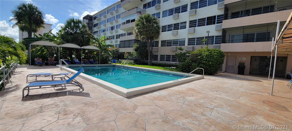 Outdoor swimming pool area with lounge chairs and adjacent multi-story building.