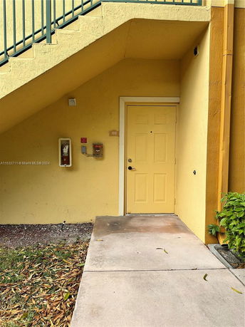 Exterior view of a yellow building entrance with stairs above.