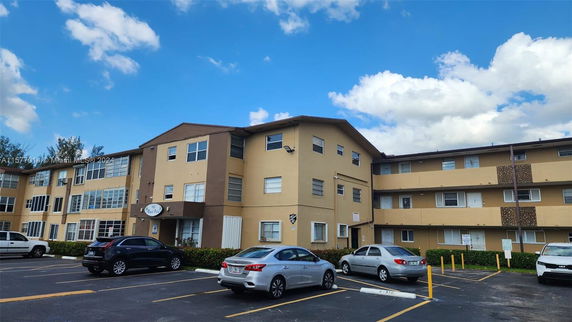 Front view of a multi-story apartment building with a flat roof and parking area.