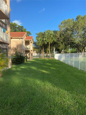Lawn area adjacent to a residential building with balconies and a white fence.
