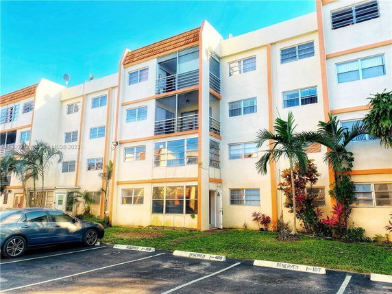 Front view of a multi-story building with a parking area and palm trees.