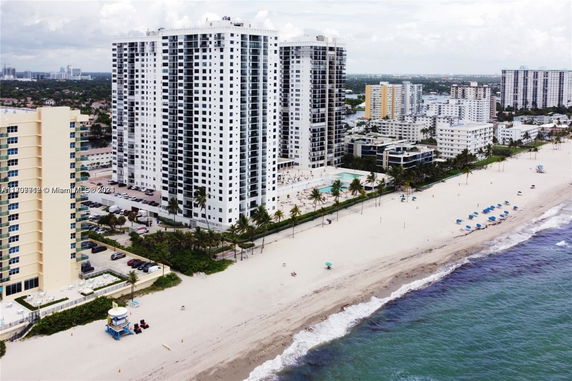 Aerial view of high-rise beachfront buildings with balconies, adjacent to a sandy beach and shoreline.