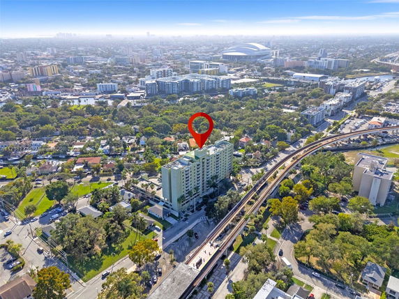 Aerial view of a tall building in an urban area with surrounding greenery and infrastructure.