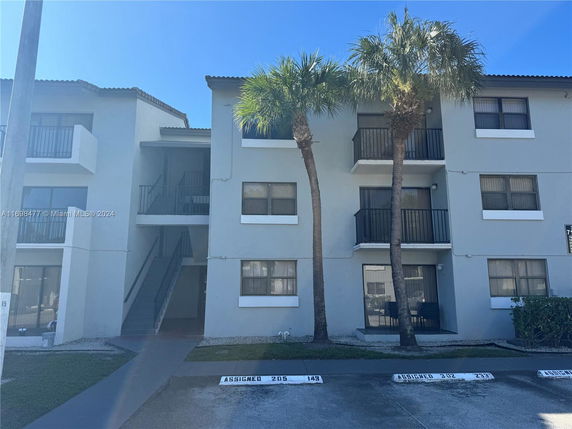 Front view of a three-story apartment building with balconies and palm trees.